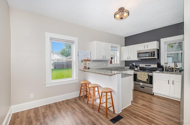 609 Coralie Ave, Hamilton, OH 45013 - kitchen with stainless steel appliances, a kitchen bar, wood finished floors, white cabinetry, and a peninsula
