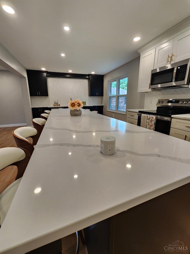 2191 Flomar Ct, Green Twp, OH 45233 - kitchen with appliances with stainless steel finishes, backsplash, light stone countertops, white cabinets, and a breakfast bar