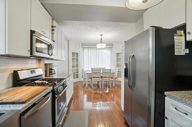 3462 Wabash Ave, Cincinnati, OH 45207 - kitchen featuring appliances with stainless steel finishes, hardwood / wood-style floors, decorative backsplash, white cabinetry, and pendant lighting