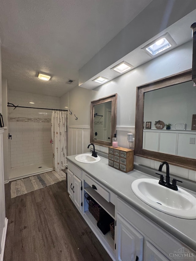 9063 Morrow Woodville Rd, Harlan Twp, OH 45162 - full bathroom with double vanity, a tile shower, wood finished floors, a textured ceiling, and a wainscoted wall