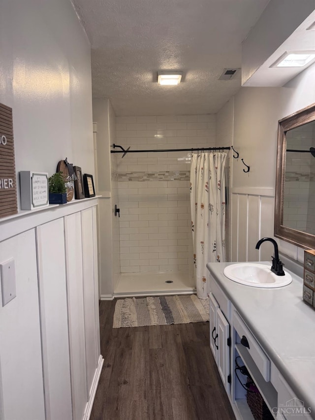 9063 Morrow Woodville Rd, Harlan Twp, OH 45162 - bathroom featuring tiled shower, vanity, wood finished floors, a wainscoted wall, and a textured ceiling