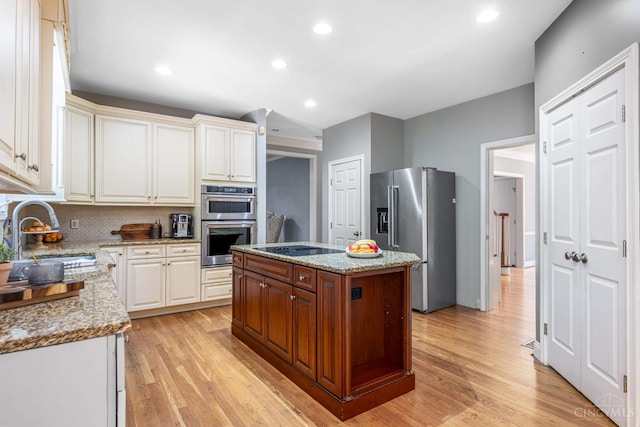 8551 Trillium Ridge Ln, Anderson Twp, OH 45255 - kitchen featuring appliances with stainless steel finishes, light wood-style floors, backsplash, light stone countertops, and a center island
