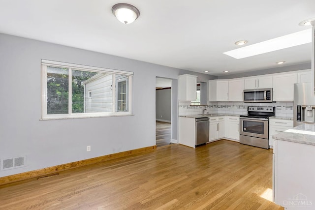 3324 Moonridge Dr, Green Twp, OH 45248 - kitchen with stainless steel appliances, a skylight, tasteful backsplash, white cabinetry, and light wood-type flooring