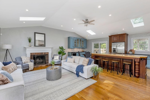 1050 Holz Ave, Anderson Twp, OH 45230 - living room featuring a skylight, vaulted ceiling, light wood finished floors, healthy amount of natural light, and a brick fireplace