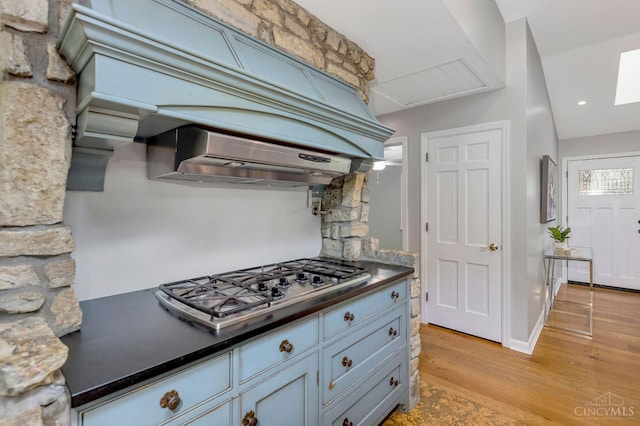 1050 Holz Ave, Anderson Twp, OH 45230 - kitchen with stainless steel gas stovetop, light wood-type flooring, dark countertops, a skylight, and ventilation hood