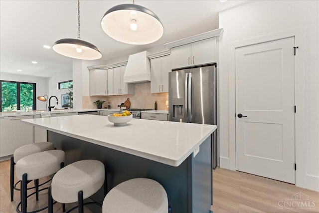 963 Windsor St, Cincinnati, OH 45206 - kitchen featuring custom exhaust hood, light wood finished floors, light countertops, decorative backsplash, and a breakfast bar area