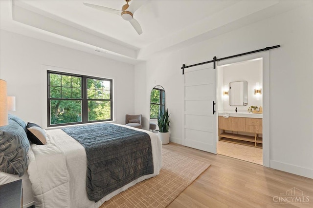 963 Windsor St, Cincinnati, OH 45206 - bedroom featuring a barn door, light wood-style floors, a raised ceiling, ensuite bath, and a ceiling fan