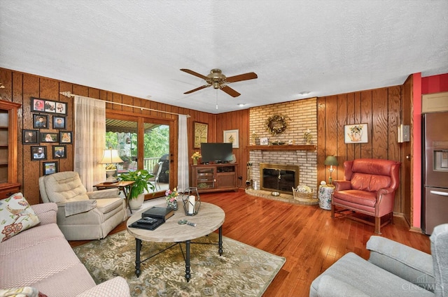 5613 Williamsburg Way, Fairfield, OH 45014 - living room with a ceiling fan, wooden walls, wood finished floors, a textured ceiling, and a brick fireplace