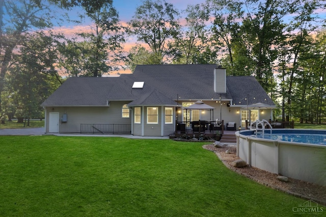 3067 Sugartree Rd, Tate Twp, OH 45106 - back of property at dusk with a deck, a gazebo, an outdoor pool, a chimney, and a lawn