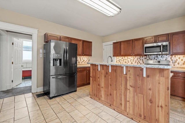 5824 Saranac Ave, Cincinnati, OH 45224 - kitchen with appliances with stainless steel finishes, tasteful backsplash, an island with sink, and light stone counters