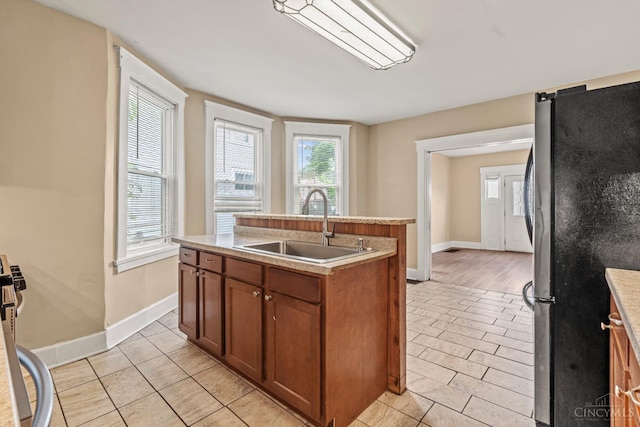 5824 Saranac Ave, Cincinnati, OH 45224 - kitchen featuring freestanding refrigerator, brown cabinets, a kitchen island with sink, light countertops, and light tile patterned flooring