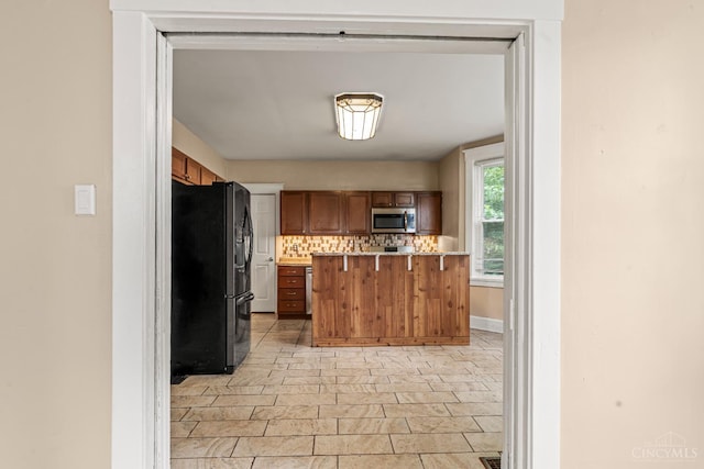 5824 Saranac Ave, Cincinnati, OH 45224 - kitchen with freestanding refrigerator, stainless steel microwave, light countertops, brown cabinetry, and a kitchen bar