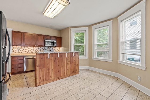 5824 Saranac Ave, Cincinnati, OH 45224 - kitchen with stainless steel appliances, tasteful backsplash, brown cabinets, a kitchen breakfast bar, and light stone counters