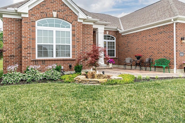 9302 W Meadow Dr, West Chester, OH 45069 - view of exterior entry featuring brick siding, a lawn, a shingled roof, and a patio area