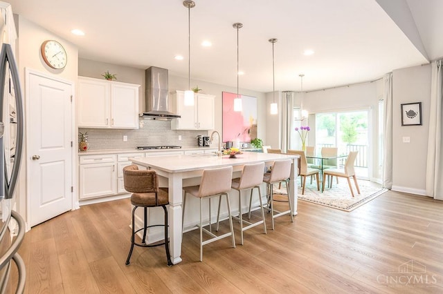 9302 W Meadow Dr, West Chester, OH 45069 - kitchen featuring wall chimney exhaust hood, a kitchen bar, light wood finished floors, appliances with stainless steel finishes, and an island with sink