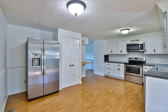 115 Treeline Ct, Harrison, OH 45030 - kitchen featuring appliances with stainless steel finishes, dark countertops, light wood finished floors, white cabinets, and a textured ceiling
