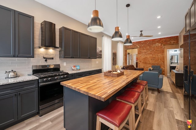 2711 Price Ave, Cincinnati, OH 45204 - kitchen featuring gas stove, wall chimney exhaust hood, open floor plan, a ceiling fan, and light wood-style flooring