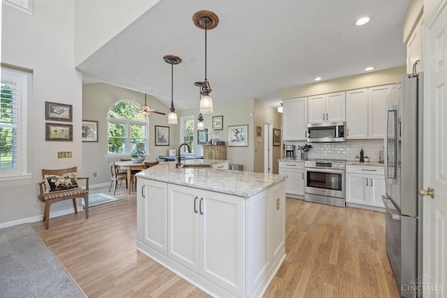 6911 Cozaddale Rd, Goshen, OH 45122 - kitchen featuring appliances with stainless steel finishes, light wood-style flooring, white cabinets, a kitchen island with sink, and light stone countertops