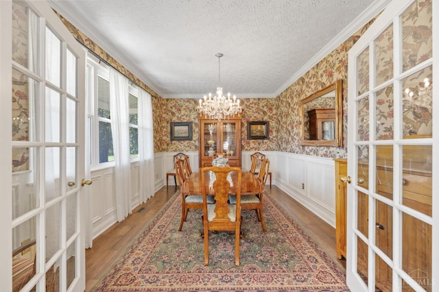 6911 Cozaddale Rd, Goshen, OH 45122 - dining area with french doors, wood finished floors, a chandelier, wallpapered walls, and crown molding