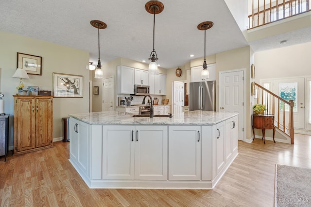 6911 Cozaddale Rd, Goshen, OH 45122 - kitchen with appliances with stainless steel finishes, light wood-style floors, white cabinetry, and light stone countertops