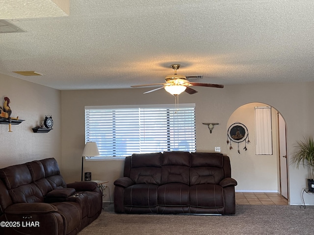 living area featuring arched walkways, light tile patterned floors, light colored carpet, a ceiling fan, and visible vents