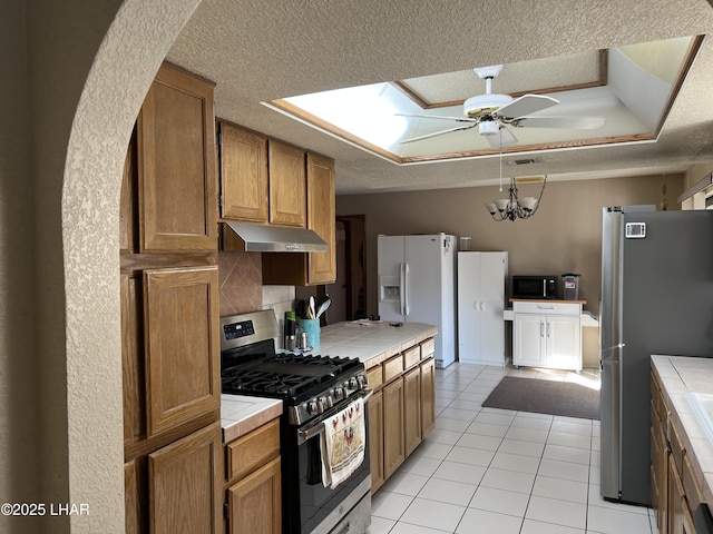 kitchen with under cabinet range hood, tile counters, stainless steel appliances, and a textured ceiling