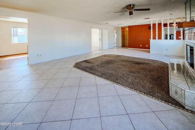 unfurnished living room featuring ceiling fan, a glass covered fireplace, a textured ceiling, and tile patterned flooring