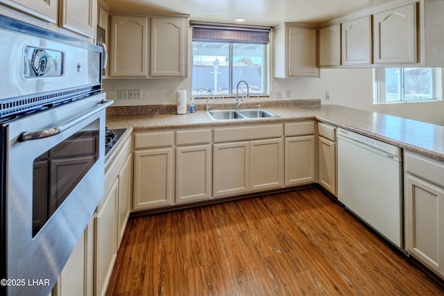 kitchen with dishwasher, wood finished floors, oven, light countertops, and a sink