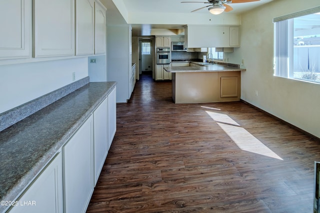 kitchen with dark wood finished floors, ceiling fan, a peninsula, stainless steel appliances, and a sink