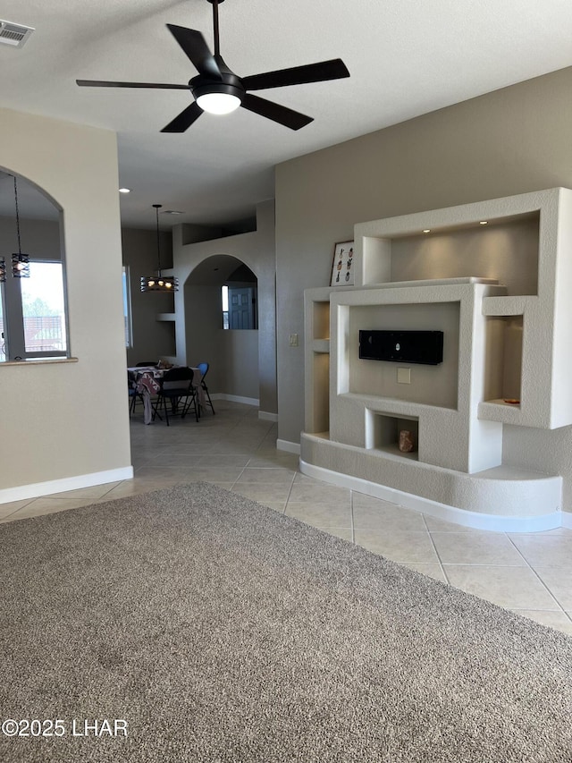 unfurnished living room featuring baseboards, visible vents, arched walkways, ceiling fan, and tile patterned flooring