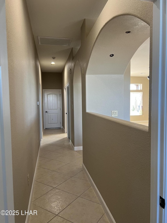 hall with light tile patterned floors, baseboards, and arched walkways