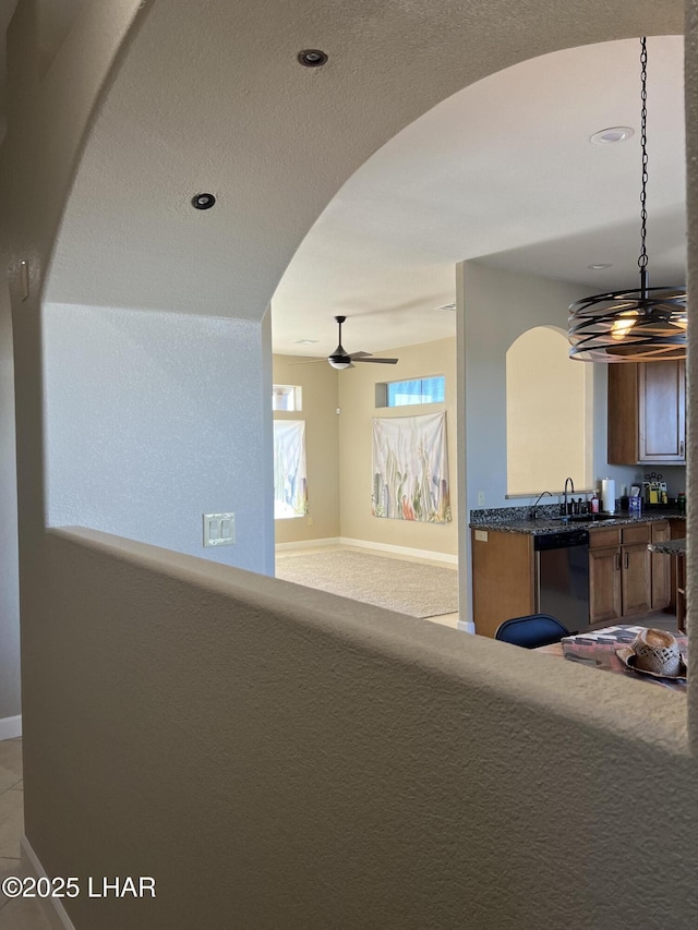 living room with arched walkways, light colored carpet, ceiling fan, and baseboards