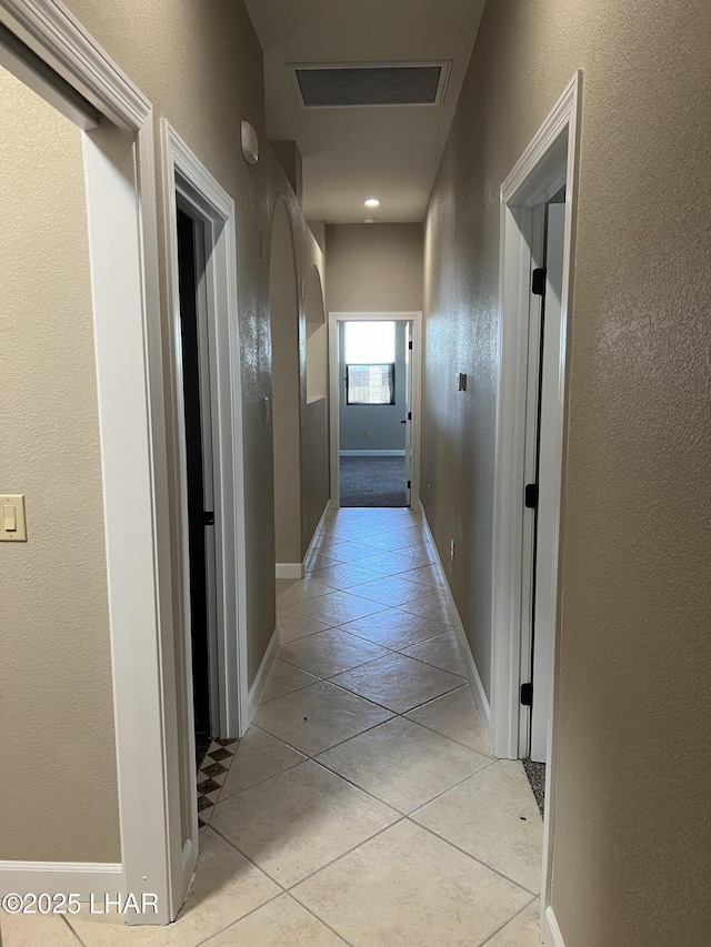 corridor with arched walkways, light tile patterned flooring, visible vents, and baseboards