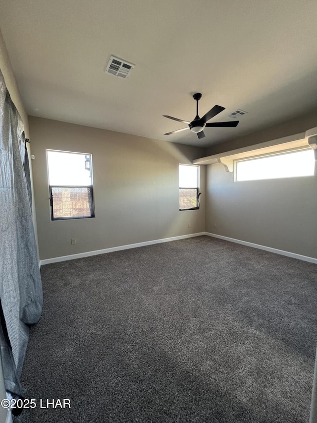 spare room featuring dark colored carpet, visible vents, and baseboards