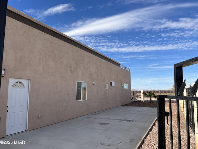 view of side of home with a patio, fence, and stucco siding