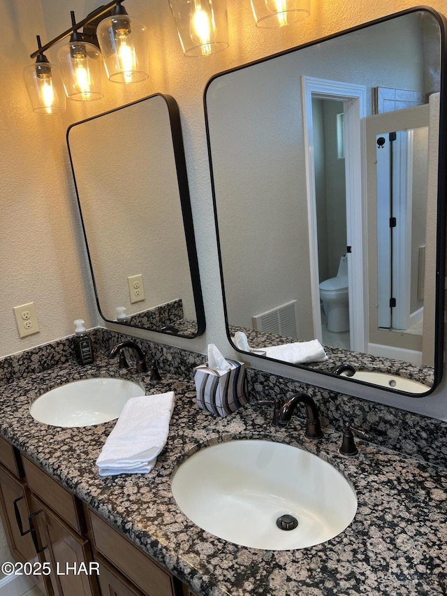 full bath featuring toilet, double vanity, a sink, and visible vents