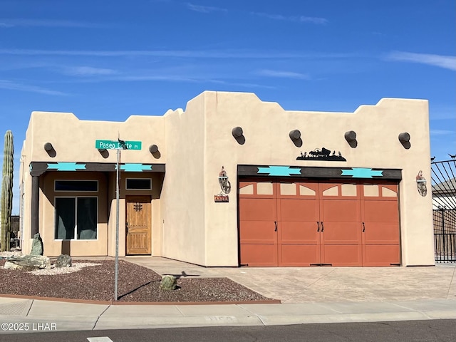 pueblo-style house featuring a garage, concrete driveway, fence, and stucco siding