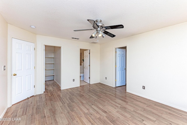 unfurnished bedroom featuring a walk in closet, light hardwood / wood-style floors, a closet, and a textured ceiling