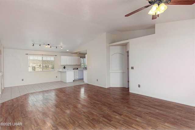 unfurnished living room with vaulted ceiling, a textured ceiling, ceiling fan, and light wood-type flooring