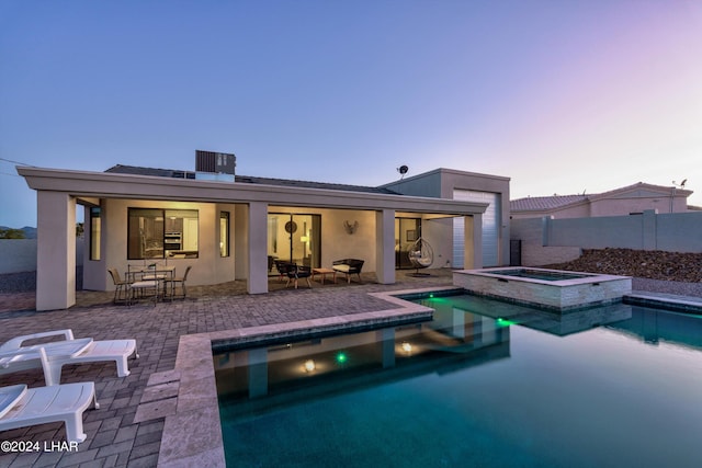 back house at dusk with central AC unit, a pool with hot tub, and a patio