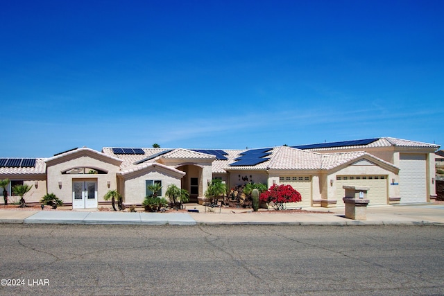 view of front facade with french doors, a tile roof, stucco siding, an attached garage, and roof mounted solar panels