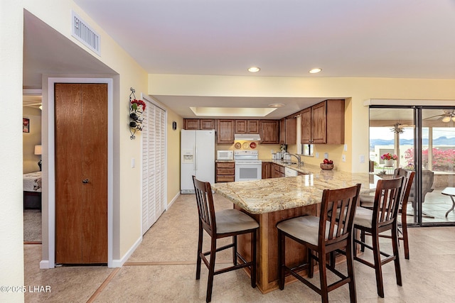 kitchen featuring white appliances, visible vents, a peninsula, light stone countertops, and under cabinet range hood