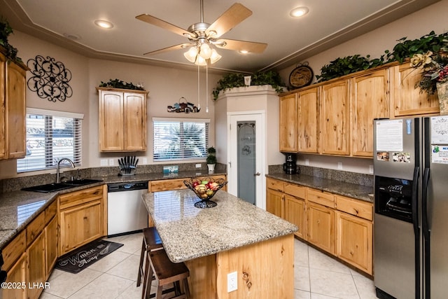 kitchen with light tile patterned floors, a kitchen island, a kitchen breakfast bar, appliances with stainless steel finishes, and light stone countertops