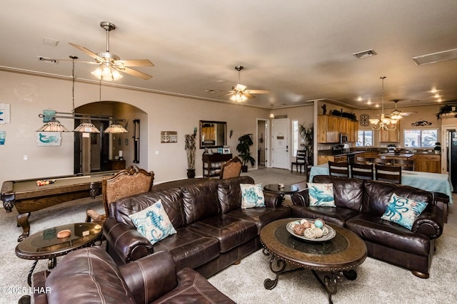 living area featuring visible vents, arched walkways, crown molding, and ceiling fan with notable chandelier