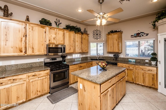 kitchen with stone counters, light tile patterned flooring, stainless steel appliances, a sink, and a center island