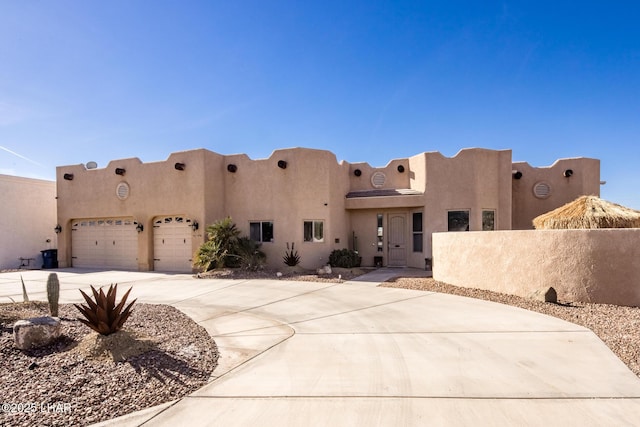 pueblo-style house with driveway, an attached garage, fence, and stucco siding