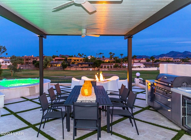 view of patio featuring ceiling fan, an outdoor fire pit, a mountain view, outdoor dining area, and an outdoor kitchen