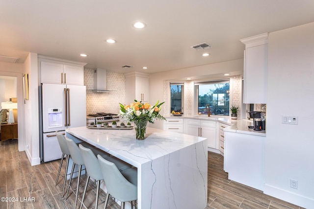 kitchen featuring visible vents, decorative backsplash, white fridge with ice dispenser, wall chimney exhaust hood, and a center island