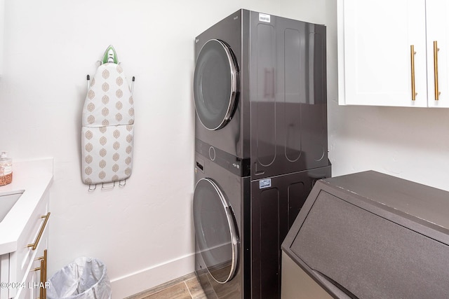 clothes washing area featuring light wood finished floors, cabinet space, stacked washer / drying machine, and baseboards