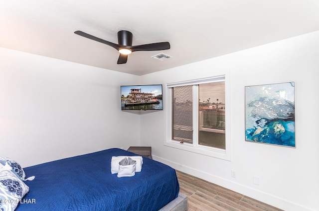 bedroom with a ceiling fan, wood finished floors, visible vents, and baseboards